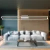 A modern living room with a long, rectangular LED ceiling light fixture mounted above a sofa and coffee table. Produktbild-Vorschau