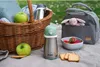 A picnic setting with a basket, food, and drinkware. Podgląd zdjęcia produktu