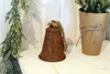 A rusty bell sits on a white shelf next to a potted plant and a frosted evergreen branch. Náhľad obrázku produktu