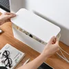 A person's hands are shown closing the lid of a white cable management box on a wooden desk. Anteprima dell’immagine prodotto