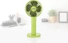 A green portable fan is placed on a white surface, with a blurred background of a desk setup. Anteprima dell’immagine prodotto