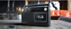 A black portable radio cassette player is placed on a wooden table in a living room setting. Voir les images du produit