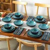 A dining table set for four people with blue and black ceramic dishes and wooden cutlery. Voir les images du produit