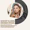 A woman applying makeup in front of a lighted mirror. Produktbild-Vorschau