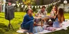 A group of friends enjoying a picnic in a backyard with a portable speaker set up. Produktbild-Vorschau