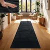 A hallway with a black runner rug on a wooden floor, flanked by plants and furniture, with sunlight streaming through a large window. Voir les images du produit