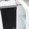 A black hanging trash can with a lid is attached to the inside of a white cabinet door. Voir les images du produit