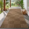 A long, brown rug with a textured pattern is laid out on a wooden deck, surrounded by lush greenery and plants. Podgląd zdjęcia produktu