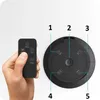 A hand holding a remote control next to a black circular device with buttons and labels. Náhled obrázku produktu
