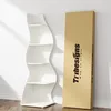 A white wave-shaped shelf unit stands next to a cardboard box with a logo and text, against a white wall. Podgląd zdjęcia produktu