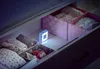 A drawer is open, showing baby items organized in baskets, with a small night light illuminating the contents. Voir les images du produit