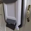 A close-up view of a white and gray foldable trash can attached to a white cabinet door with a decorative brass and ceramic handle. Náhľad obrázku produktu