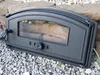 A black cast iron oven door with a glass window, resting on a bed of gravel with stones in the background. Náhľad obrázku produktu