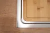 A close-up view of a wooden cutting board integrated into a stainless steel sink. Produktbild-Vorschau