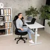 A woman is sitting at a desk in an office environment, talking on the phone. Produktbild-Vorschau