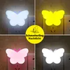 A collage of four images showing butterfly-shaped LED night lights plugged into wall sockets, each in a different color. Produktbild-Vorschau