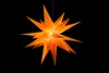 A bright orange star-shaped lantern hangs against a black background. Produktbild-Vorschau