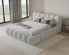 A modern bedroom with a large, upholstered bed as the focal point, featuring large windows with curtains and a view of greenery outside. Voir les images du produit
