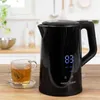 A black electric kettle with a digital display is shown on a wooden table next to a glass of tea. The background is a kitchen setting. Náhled obrázku produktu