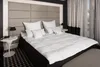 A neatly made bed with a large duvet and several pillows, set against a padded headboard in a bedroom setting. Produktbild-Vorschau