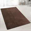 A shaggy brown rug is laid out on a light-colored wooden floor in a room with white curtains and a white side table. Náhled obrázku produktu