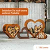 Several heart-shaped metal log holders filled with firewood are displayed in front of a rustic wooden wall. An orange banner with German text is overlaid on the top left. Produktbild-Vorschau