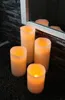 Four LED candles are arranged on a dark rug in front of a stone-patterned wall and a mirror. Podgląd zdjęcia produktu