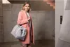 A woman stands in a modern building hallway, holding a duffel bag. Produktbild-Vorschau