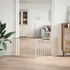 A wooden pet gate is set up in a doorway, separating two rooms in a home. One room has a plant and a cabinet, while the other has a sofa and a cabinet. Podgląd zdjęcia produktu
