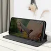 A black flip case for a smartphone is shown standing upright on a wooden surface, displaying a video of someone playing a guitar. Produktbild-Vorschau