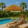 A woman relaxes on a lounge chair under a straw umbrella next to a swimming pool. Voir les images du produit