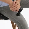 A person is using a black massage gun on their thigh while sitting. Produktbild-Vorschau