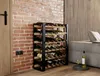 A wine rack filled with wine bottles is placed against a brick wall next to a sofa. A bottle of white wine and a glass are on a small table in the foreground. Produktbild-Vorschau