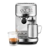 A silver Sage Bambino Plus espresso machine with a glass of espresso and a milk frothing pitcher. Produktbild-Vorschau