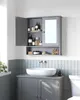 A gray bathroom cabinet with a mirror and open doors, displaying various toiletries. Below the cabinet is a white sink on a gray vanity. The wall is tiled with light blue vertical tiles. Náhled obrázku produktu