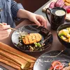 A person is eating from a black and gold marbled plate with a pastry and fruit. Náhľad obrázku produktu
