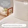 A close-up view of a white duvet cover and pillow on a bed, with a small bench with decorative items in the background. Voir les images du produit