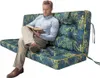A man is sitting on a large cushion with a floral pattern, reading a book. Anteprima dell’immagine prodotto