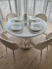A round white dining table with four beige chairs and placemats with bowls set for a meal. Voir les images du produit