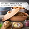 A close-up shot of terracotta bread baking dishes, one with a loaf of bread inside, and a sliced bread roll with butter and jam on a wooden board. Produktbild-Vorschau