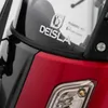 A close-up view of the front of a red and black three-wheeled vehicle, showing a logo and certification sticker on the windshield. Produktbild-Vorschau