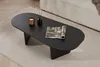 A black oval coffee table with a magazine, candle, and diffuser on it, placed on a rug next to a sofa. Voir les images du produit