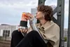 A woman sitting on a bridge structure, holding a portable blender with a colorful drink inside. Voir les images du produit