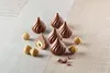 A collection of chocolate pralines and hazelnuts arranged on a light wooden surface. Produktbild-Vorschau