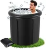 A man is sitting in a black inflatable ice bath filled with ice and water, with ice cubes splashing around him. The bath is placed on a patch of green grass. Produktbild-Vorschau