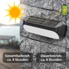 A solar-powered wall light is mounted on a stone wall, with an illustration of the sun charging the device and a battery icon indicating charge. Produktbild-Vorschau