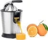 A stainless steel electric citrus juicer is shown in operation, with fresh orange juice pouring into a glass. Two whole oranges and one half-orange are placed next to the juicer. Náhľad obrázku produktu
