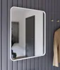 A mirror with a white frame hangs on a gray paneled wall next to a coat rack with a tan jacket. Produktbild-Vorschau