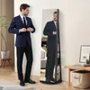 A man in a suit is adjusting his jacket in front of a full-length mirror that is part of a jewelry cabinet. Produktbild-Vorschau