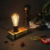 A vintage-style desk lamp with an exposed Edison bulb sits on a textured surface, surrounded by decorative elements like dried flowers and a miniature car. Produktbild-Vorschau